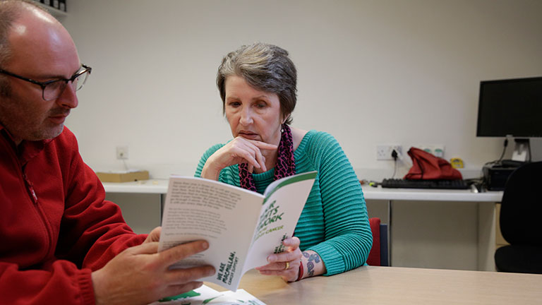 Cath reads a Macmillan booklet with her manager at her workplace. The booklet is about her rights at work. 