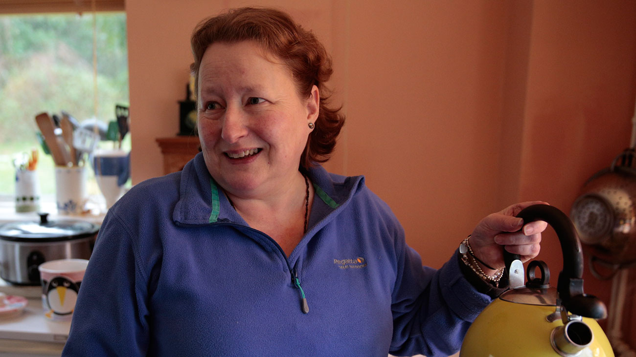 Clare holds up a yellow kettle. She is making tea in her kitchen.