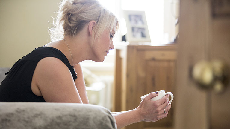 Leigh sits on her sofa holding a cup of tea