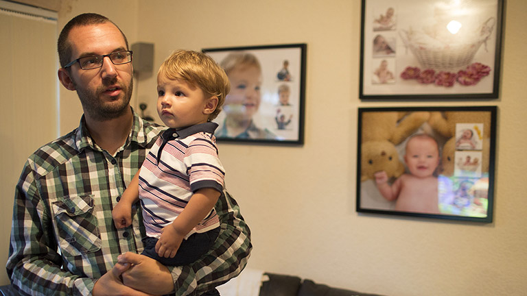 Luke holds his son in the living room 