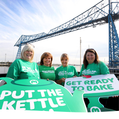 Supporters wearing green tshirts and holding placards 'get ready to bake', smiling beneath the Transporter Bridge in Middlesbrough.