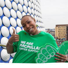 A supporter smiling with her thumb up, holding a large green foam finger in front of the Bull Ring, Birmingham.