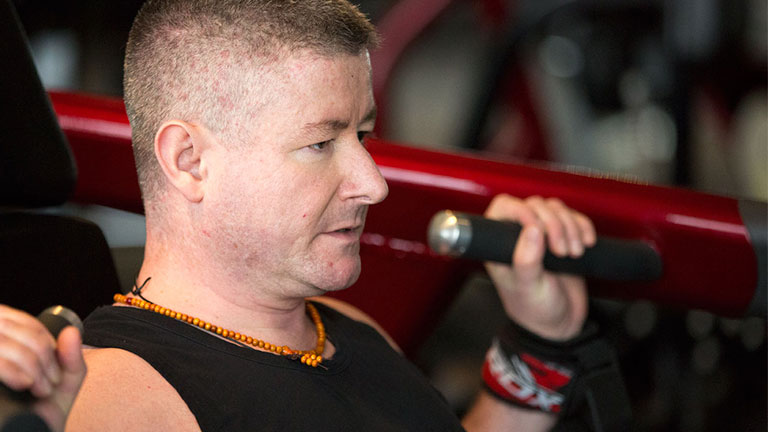 A man (Anthony) sits side-on in a gym setting. He is using gym apparatus.