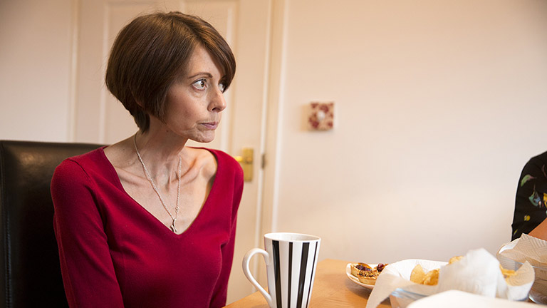 Claire drinks a cup of tea at a table