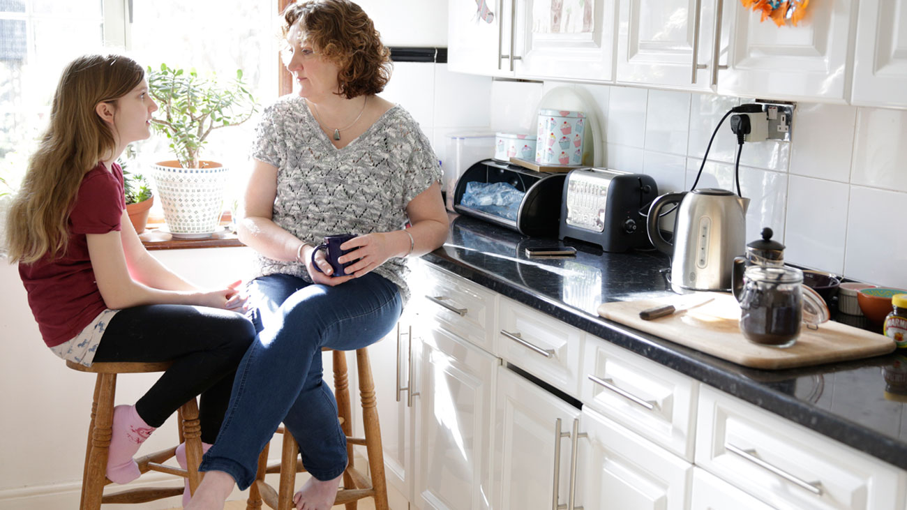 Daloni and her young daughter sit facing each other in her kitchen. The kitchen is full of sunlight.