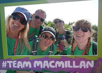 Five Macmillan fundraisers posing behind a cardboard picture frame which says #teammacmillan.