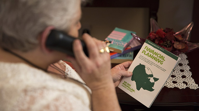 Philomena calls the Macmillan Support Line. She is holding a Macmillan leaflet about finances.