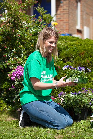 A blonde woman in a Macmillan t-shirt kneels while gardening