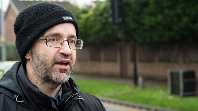 A photograph of Kris, who was diagnosed with liver cancer and then non-Hodgkin lymphoma. He's standing by the road talking.