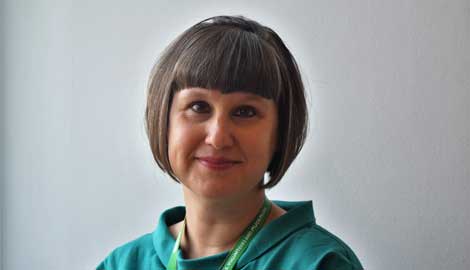 A woman with short black hair and a fringe looks at the camera