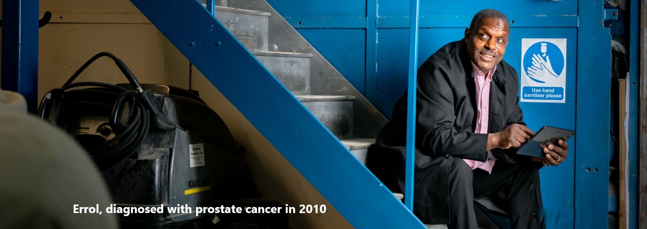 Errol, diagnosed with prostate cancer in 2010, sitting on the stairs and holding an tablet device.