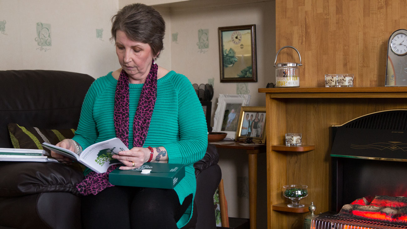 Cath reads a Macmillan booklet. She is seated in a chair in her home.