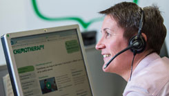 A profile of a Macmillan employee who is wearing a telephone headset, and facing a computer screen with the screen on a chemotherapy webpage.