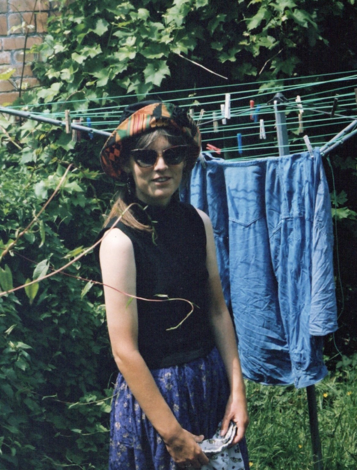 Young woman wearing a hat and sunglasses standing by a washing line.