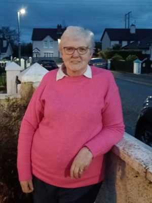 Daphne is pictured outside and is leaning against a fence. She is looking at the camera and wearing a bright pink jumper.