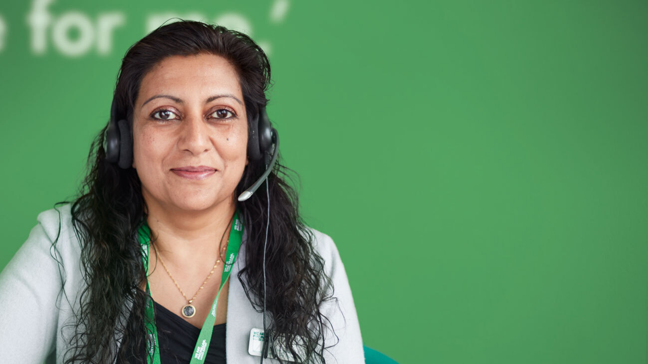 Maria, a Cancer Info & Support Officer in her 40s, wearing a headset.