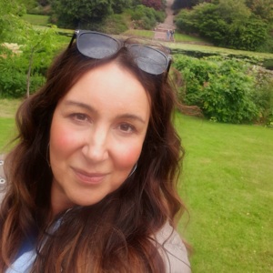 A selfie of Sara. She appears outside and is looking at the camera. On top of her head are a pair of black sunglasses.