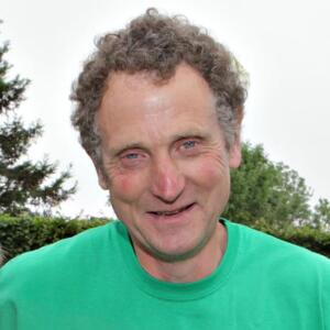 Andrew is looking at the camera and smiling. He is wearing a bright green Macmillan t-shirt and has curly brown hair.