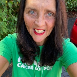 A selfie of Sonia where the camera is angled up. She is looking up at the camera and smiling. She is wearing a green Macmillan tshirt. 