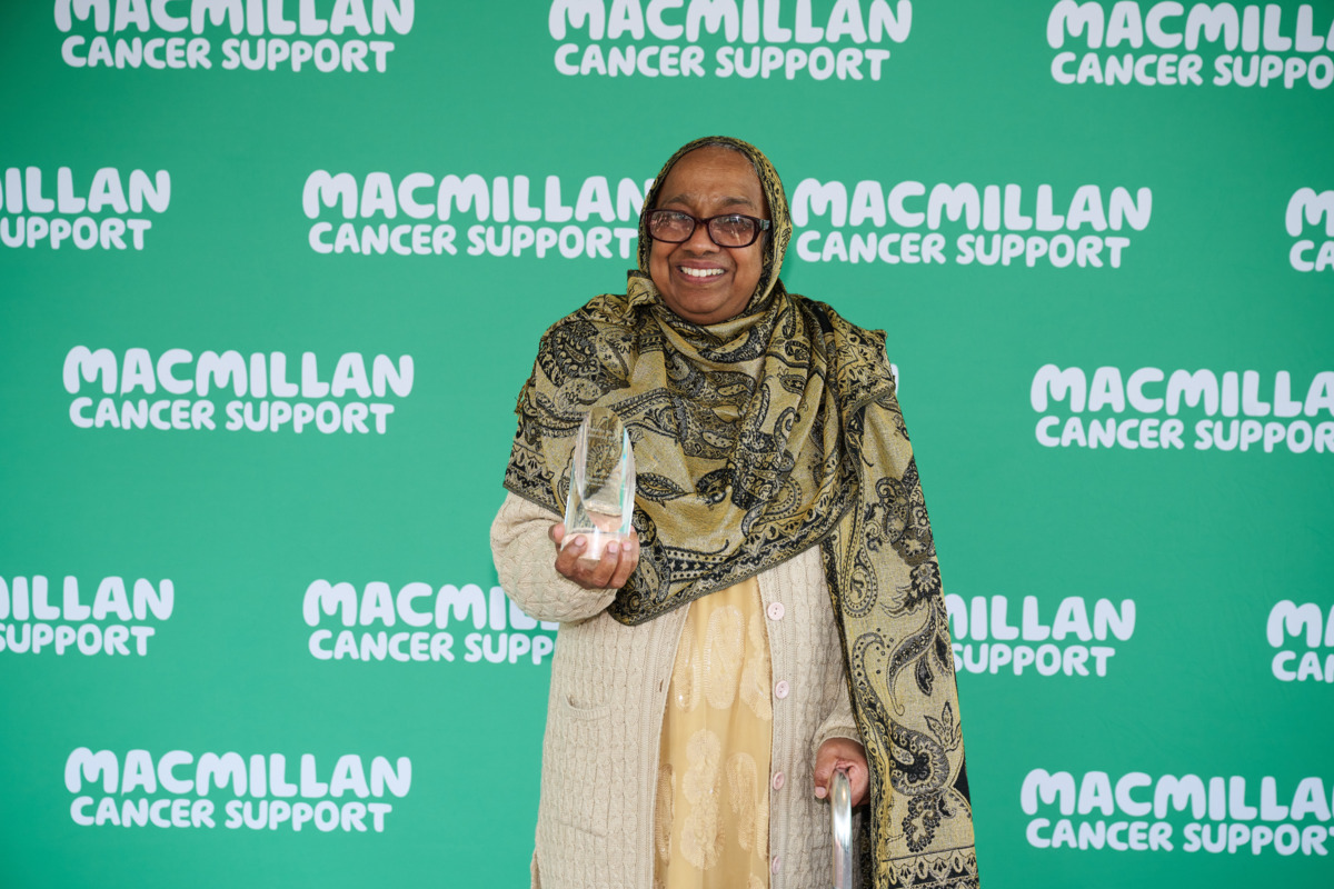 Sarifa is smiling at the camera. She is wearing a brown and gold headdress. In her hand she is holding a clear glass award. 