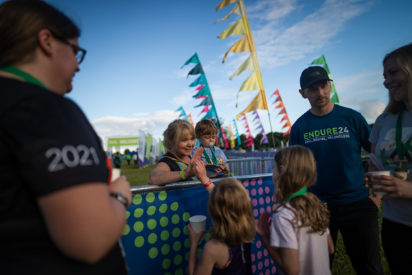 A person is standing behind a barrier. They are putting up their hand to high five two young people on the other side of the barrier.