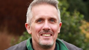 Palliative Care Clinical Nurse Specialist Andrew, smiling while looking at camera wearing green Macmillan fleece