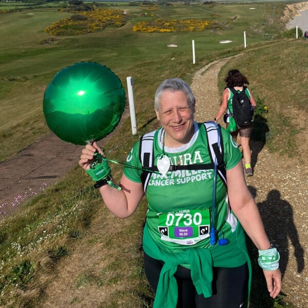 Laura is walking by the coast in a green Macmillan t-shirt.