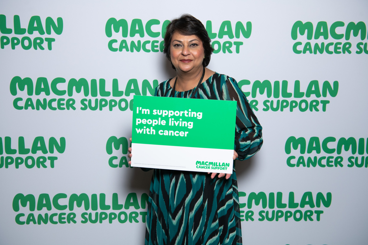 A south Asian lady with brown hair with a sign supporting people with cancer .