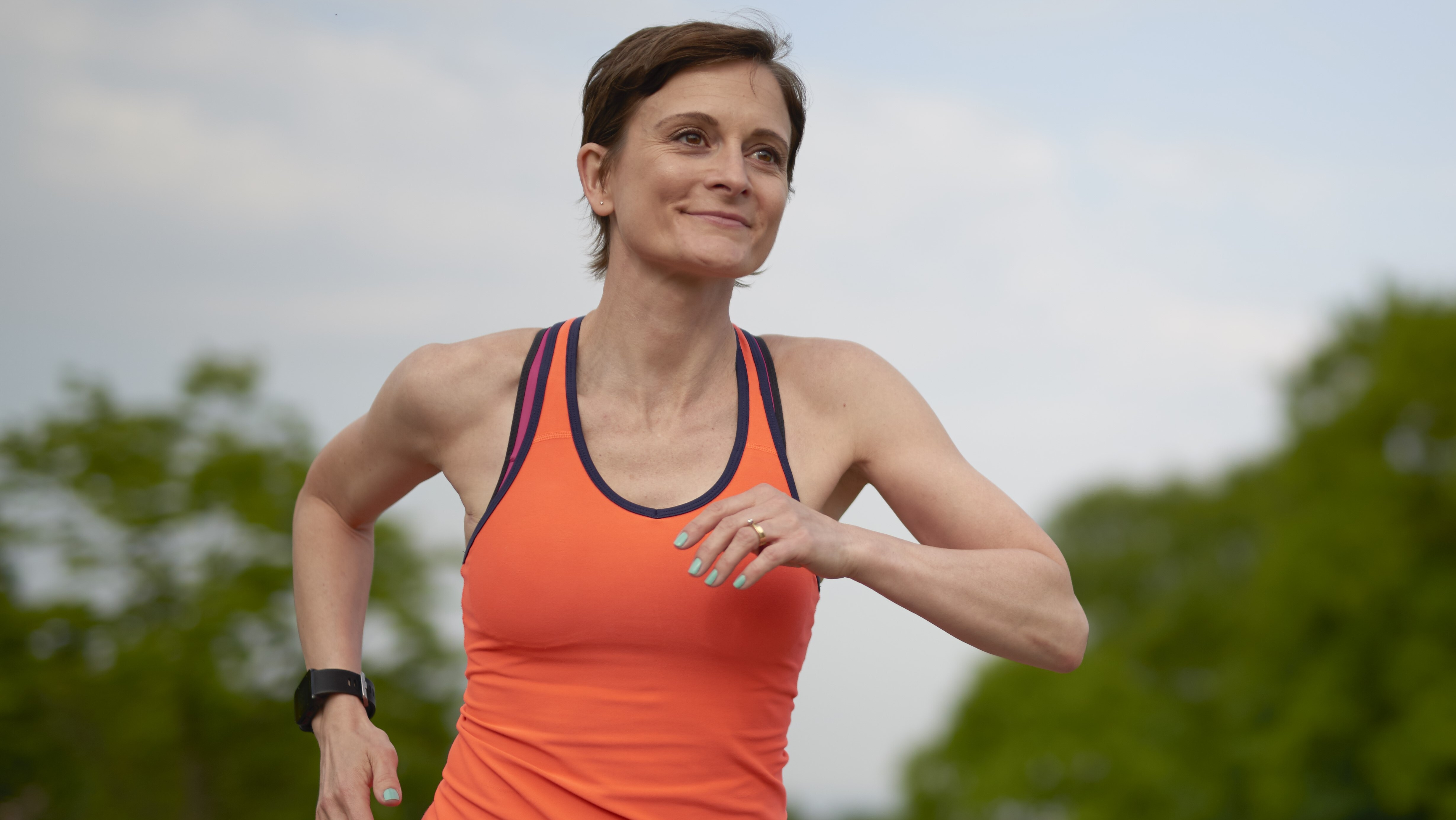Woman in orange vest out for a run in a park.