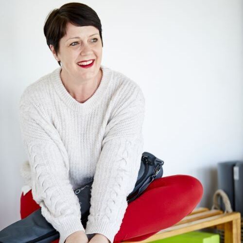 Woman sitting on bench wearing cream jumper smiling away from camera.