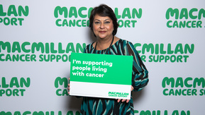 A south Asian lady with brown hair with a sign supporting people with cancer .