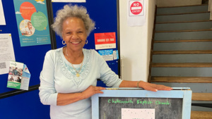 Shirley standing next to a Coffee Morning this way sign.