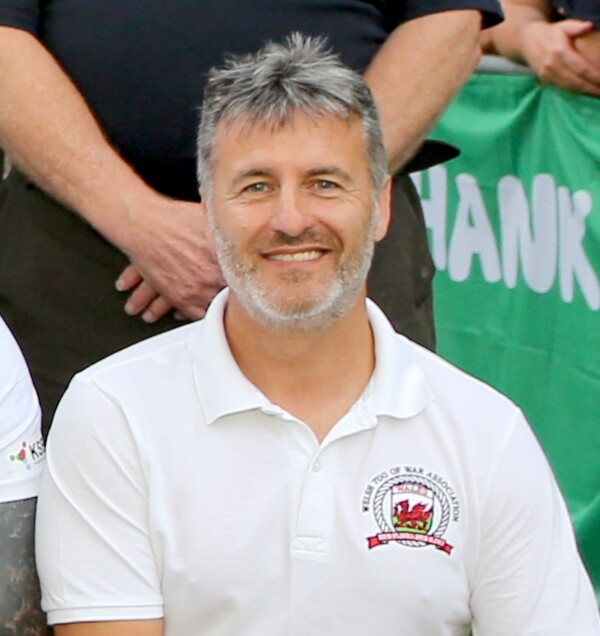 Gareth has short hair and is wearing a white top. He is seen from the chest up.