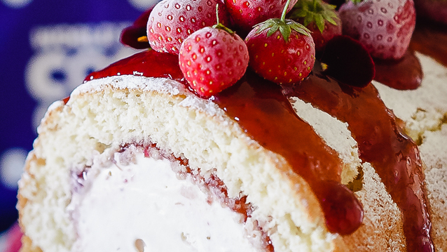 A classic arctic roll featuring a spiral of soft sponge cake wrapped around creamy vanilla ice cream, topped with glossy strawberry jam and garnished with fresh strawberries.