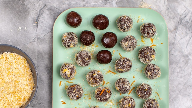 Several truffles are placed on a mint green plate. The truffles are covered in chocolate, and some have a sprinkle of desiccated coconut. Next to the plate is a bowl of desiccated coconut.