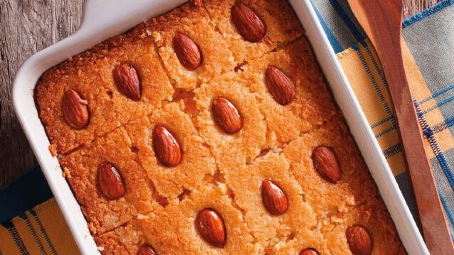 A golden tray of basbousa—soft, buttery semolina cake soaked in fragrant rose and lemon syrup—topped with whole almonds. Its rich, nutty texture and syrupy sweetness make every bite irresistible.