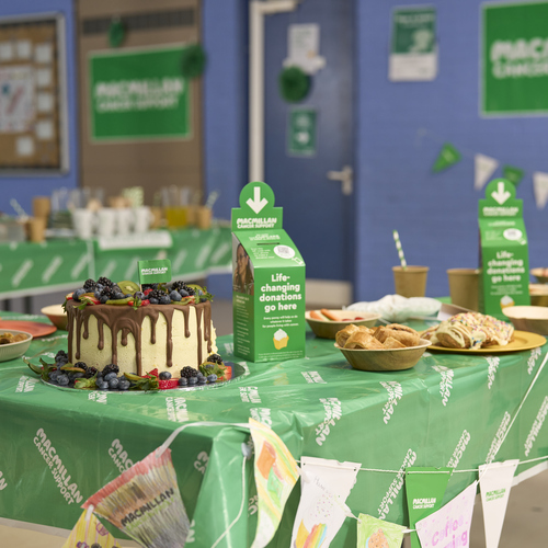 A table in a school covered with a green tablecloth and baked goods.