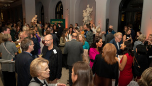 Several people are standing in a large hall. They are talking to each other in groups. They appear to be at an event.