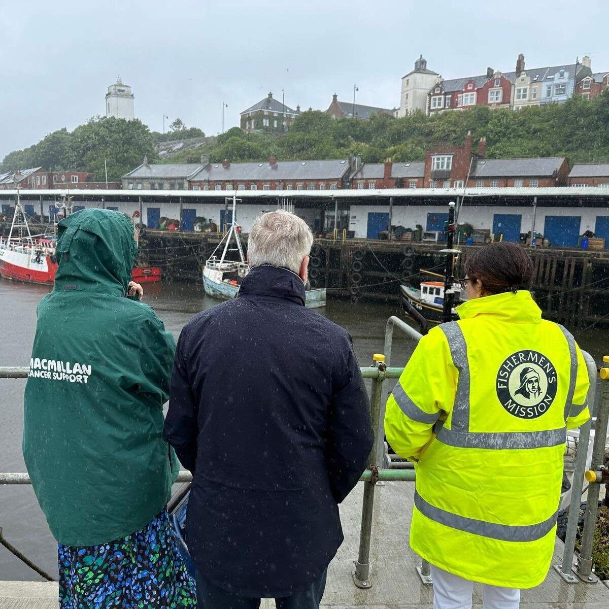 A photo of three people looking at at boats on the water. They're backs are to the camera.