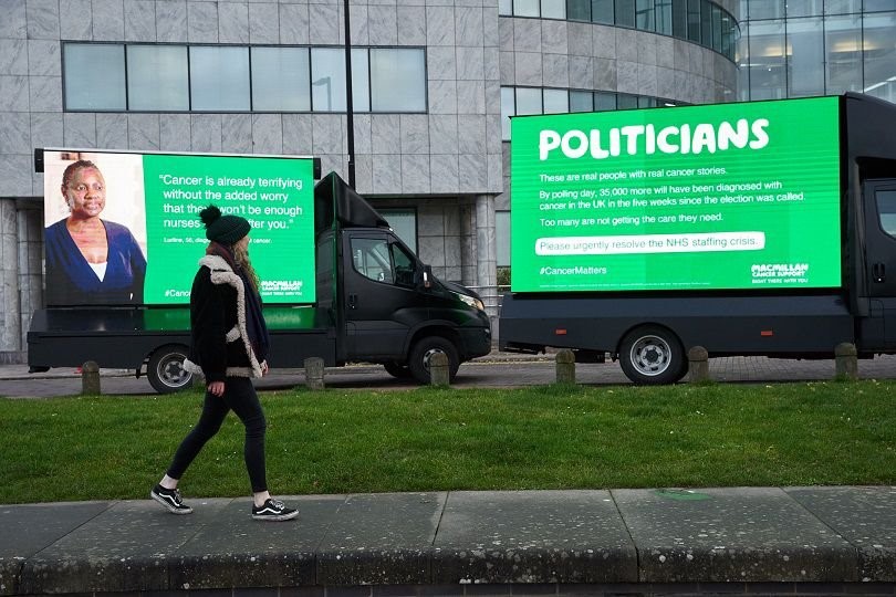 A person walking on a sidewalk next to a large green sign 