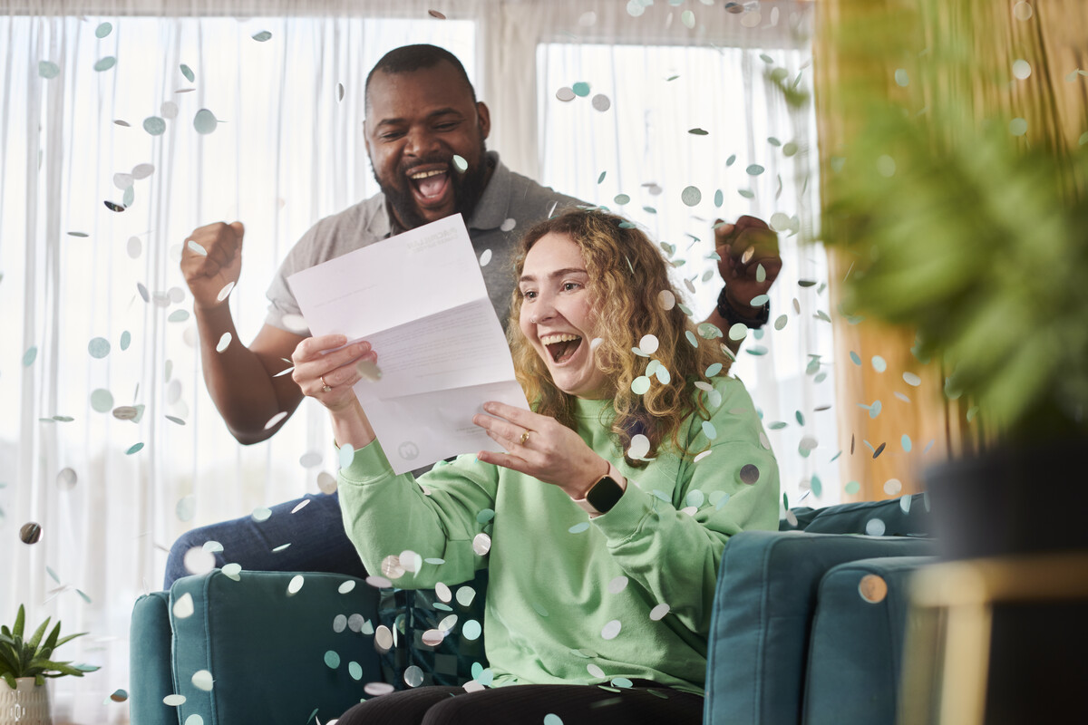 A man and a woman cheering having read a letter saying they've won the raffle. Confetti flies around them.