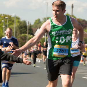 A Macmillan runner with his hand held out for a high five from a boy watching the race
