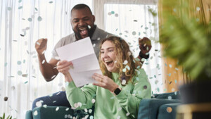 Two people are looking really excited as they read a letter. There is confetti falling around them.