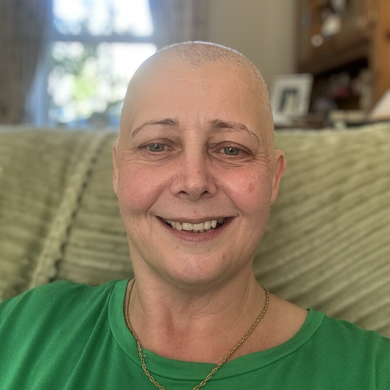 A selfie of Stephanie. She is sitting on a beige sofa. She is smiling and is wearing a green top.
