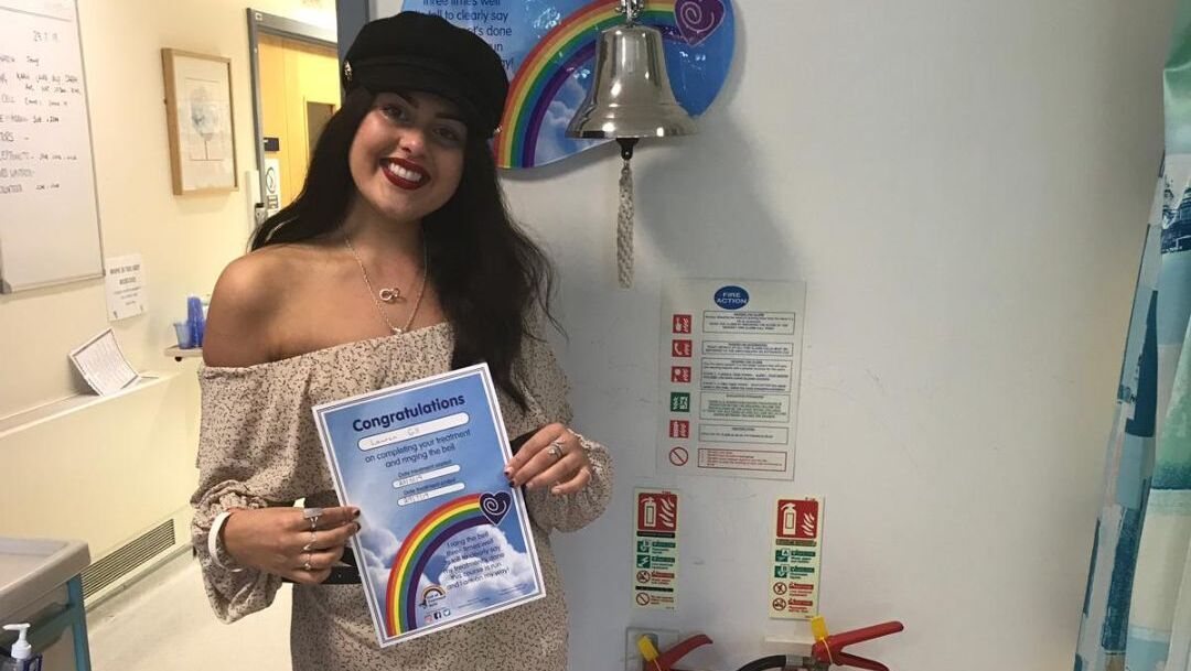 A young woman with long dark brown hair holds a certificate showing she has finished cancer treatment.