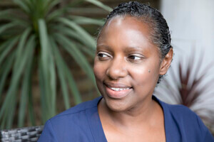 A woman with short, curly black hair is smiling and looking to the side. She is wearing a navy blue top.