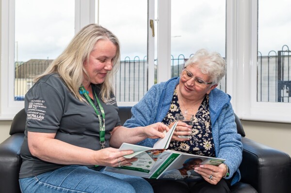 A link worker from CRT together is with a client. They are looking at a Macmillan Cancer Support booklet together. 