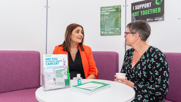 Ann Broadway, development manager talking to someone about the CTR Together project. They're sitting at a table with cancer information booklets and posters around them.