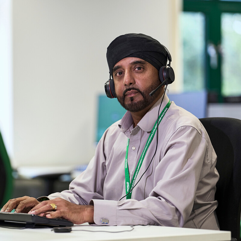 Akbal Suryavansi is an Energy Advisor at Macmillan. He is wearing a light purple shirt and a dark dastar (turban, pagri). He has a headset on and is typing on a computer keyboard.