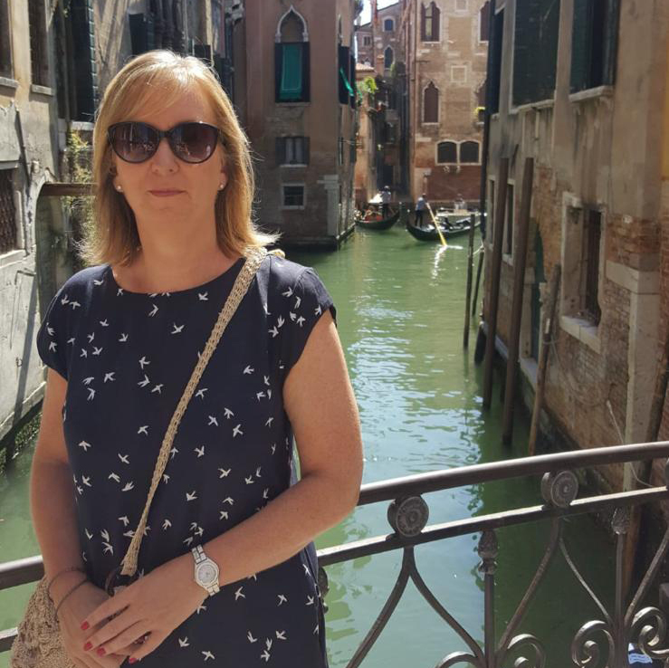 A woman wearing sunglasses, standing on a bridge over a canal in Venice.